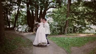 公园里的时髦新娘和新郎。 新郎把新娘抱在怀里，绕来绕去。 快乐的恋人分享婚礼日。
